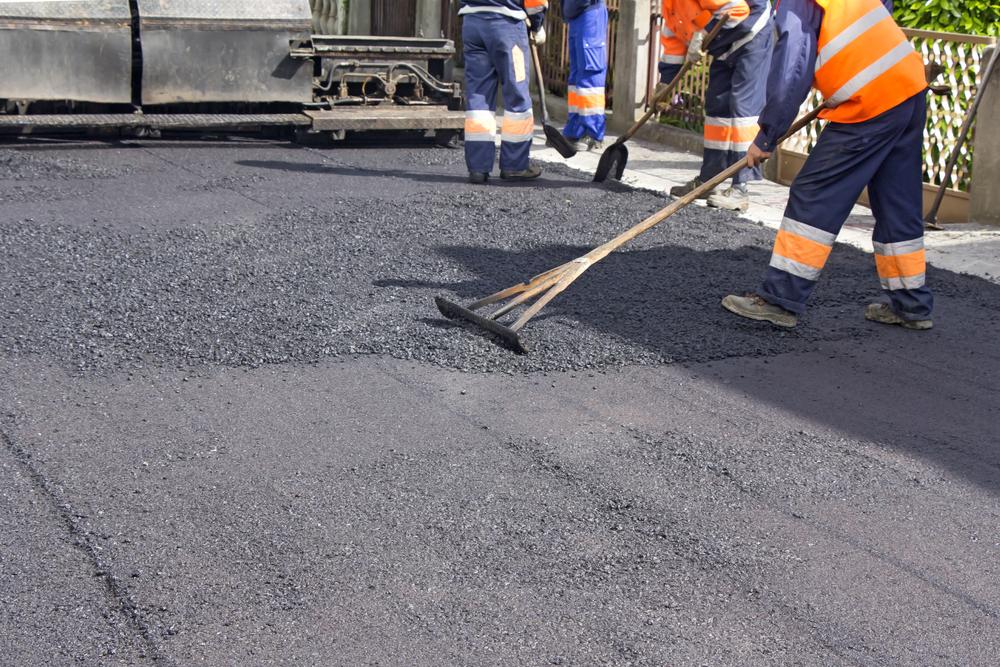 A worker in a safety jacket smoothing out concrete on a road