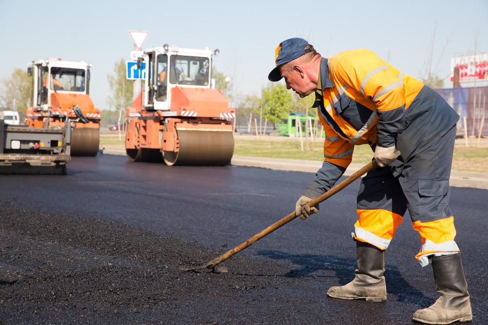 A man smoothing gravel along a road, pavers in the background